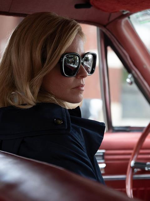 Elizabeth Banks wearing big sunglasses in a vintage car with red leather interior